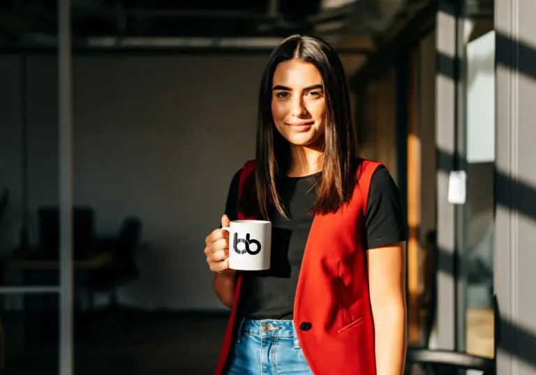 Woman in black shirt and red sleeveless vest holding a mug with Baden Bower mug smiling.
