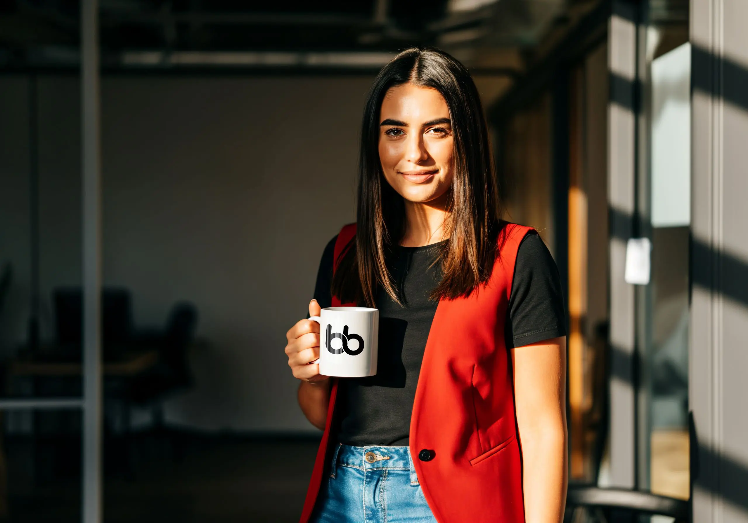 Woman in black shirt and red sleeveless vest holding a mug with Baden Bower mug smiling.